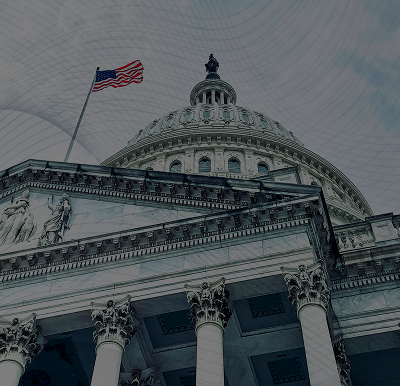 Low-angle view of the U.S. Capitol building's dome and columns with an American flag waving on a pole.
