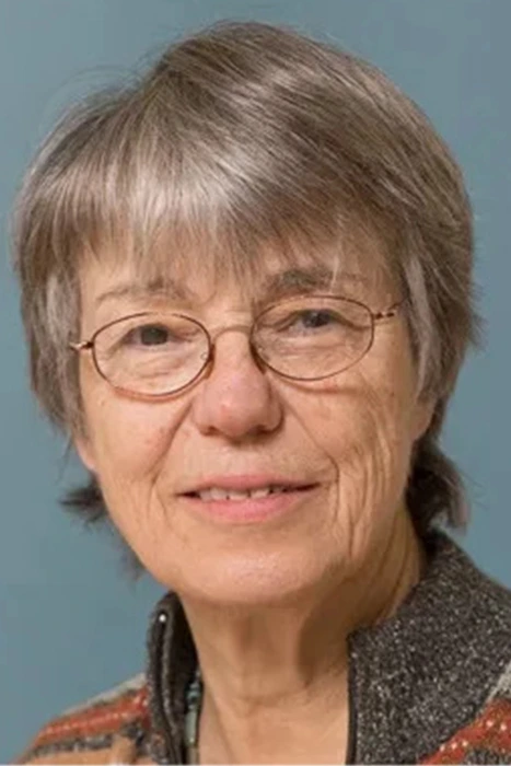 Jen Porter 2 An older woman with short gray hair and glasses smiles slightly, wearing a patterned sweater against a blue background.