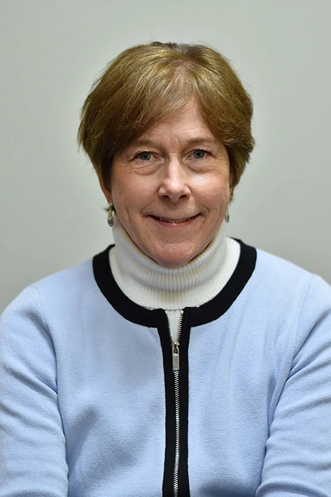 Lucy Painter A person wearing a light blue cardigan with a white turtleneck underneath, posing against a plain background.