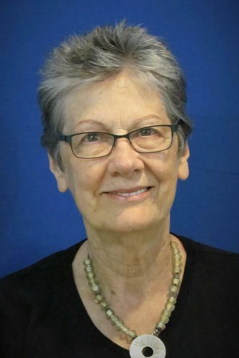 Margaret Babb A woman with short gray hair and glasses, wearing a necklace and a black top, smiles against a blue background.