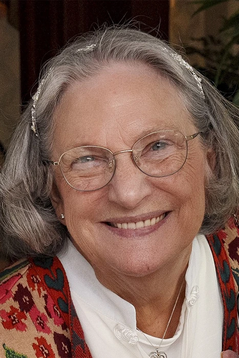 Ross&RussWedding_(2024_04_27)_0289 V2 Elderly woman with gray hair and glasses smiling, wearing a colorful patterned garment and a headband.